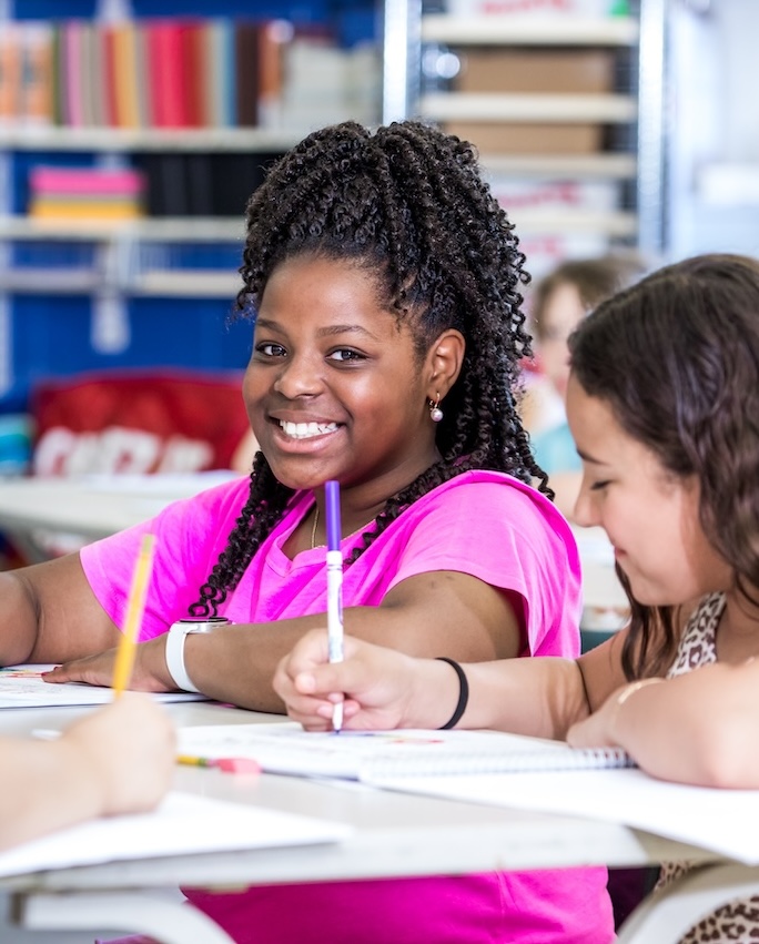 a young black girl smiling for the camera at her desk in the classroom a young black girl smiling for the camera at her desk in the classroom